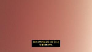 Ein Farbverlauf von pink zu beige füllt den Bildschirm. Ein Untertitel erscheint auf dem unteren Teil des Bildes, dort steht: “Some things are too close to be shown.” (zu Deutsch: „Manche Dinge sind zu nah, als dass man sie zeigen könnte“.)