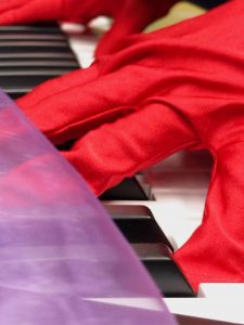 Zwei Hände in roten Handschuhen berühren die Tastatur eines Klaviers.