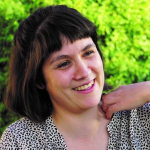 Porträt der Comiczeichnerin und Autorin Christiane Haas. Sie trägt eine gemusterte Bluse und lächelt schräg an der Kamera vorbei.
