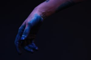 Blau-lila gefärbte Hand vor schwarzem Hintergrund.