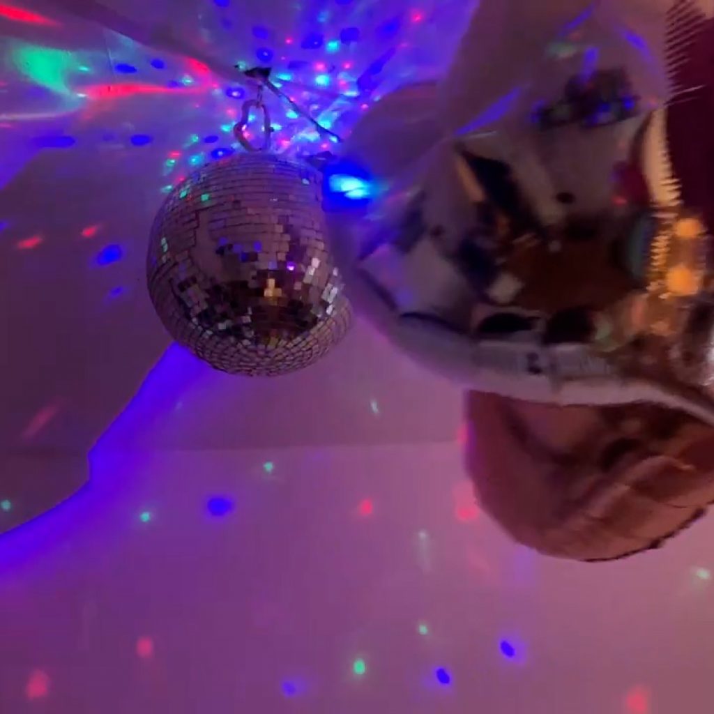 Auf dem Foto sind Details einer Partybeleuchtung – Wände und Decke mit Discokugel – aufgenommen. Vorne hängt ein großer silberfarbener Herzluftballon.